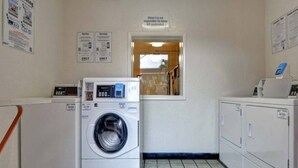 A laundry room with a front-loading washing machine, a dryer, and a sign indicating the motel is not responsible for unattended items. - 2 Full Beds|Mini Fridge,Smoking (Dania Beach)