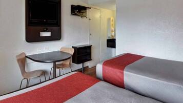 A hotel room with a bed, a desk, a chair, and a television.