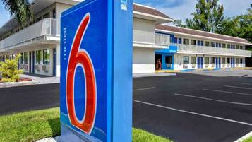 Een motel met een opvallend bord met het cijfer '6', een parkeerplaats en een gebouw met meerdere ramen en balkons.