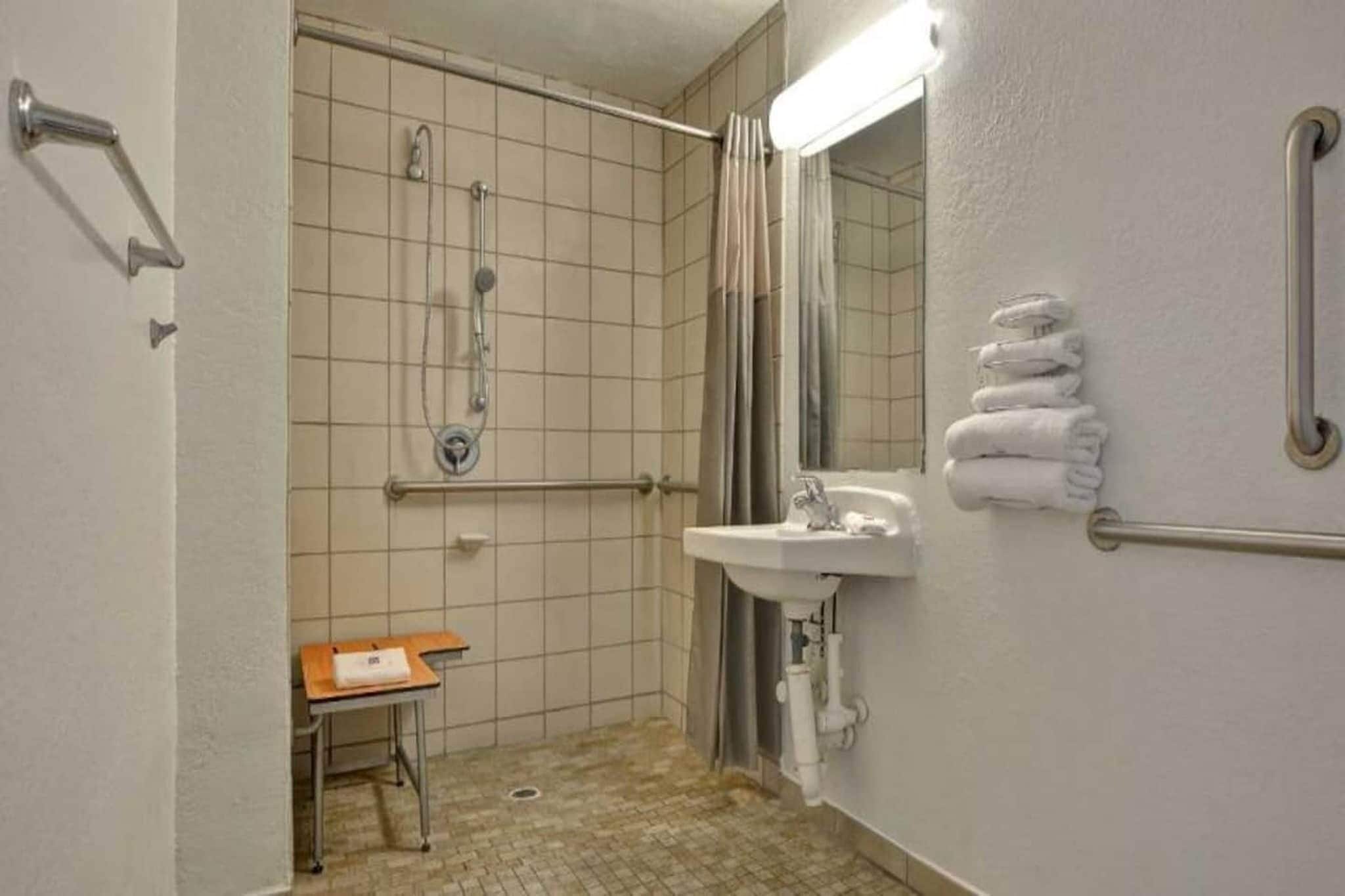 A bathroom with a shower, a sink, a mirror, a towel rack, and a small table.