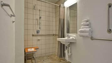 A bathroom with a shower, a sink, a mirror, a towel rack, and a small table.