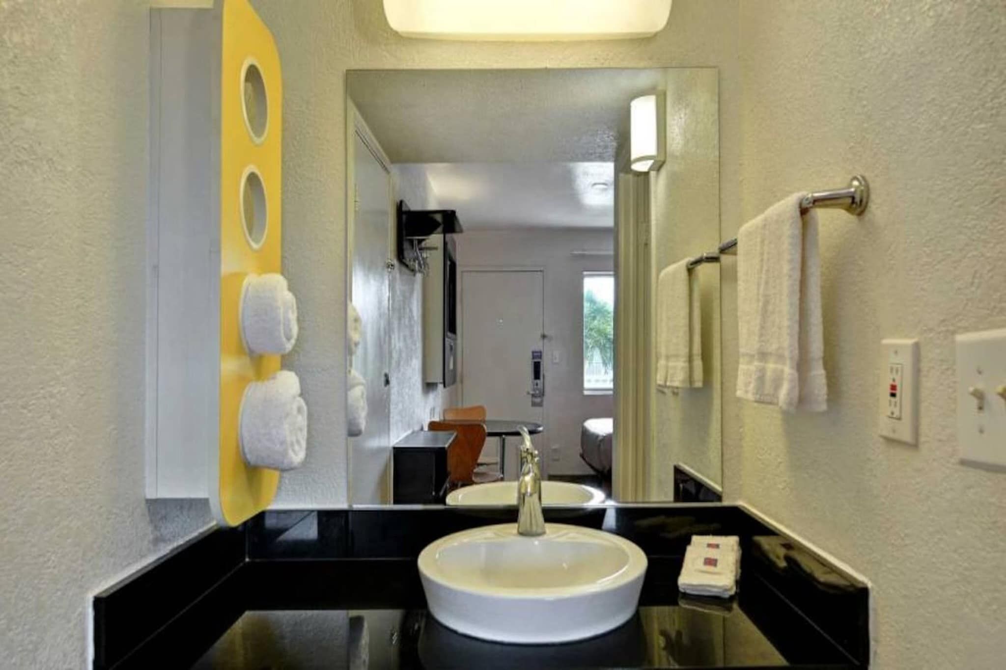 A hotel bathroom with a black countertop, a white sink, and a mirror.