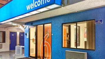 Een blauw gebouw met een 'welcome'-bord, glazen deuren en een 'busje toegankelijk'-bord.