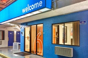 Ein blaues Gebäude mit einem 'Welcome'-Schild, Glasüren und einem Schild, das barrierefreien Zugang für Rollstuhlfahrer kennzeichnet.