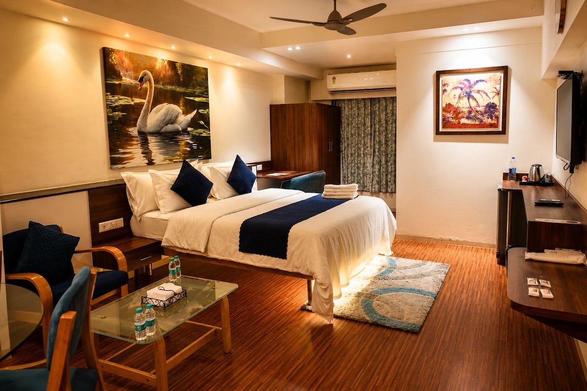 A hotel room with a bed, a desk, a chair, a TV, and artwork on the walls.