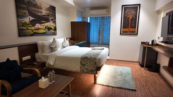 A hotel room with a bed, bedside table, a desk, a chair, a TV, and artwork on the walls.