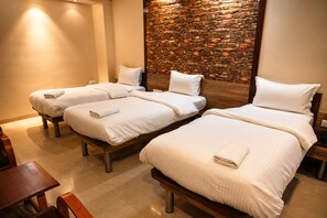 A hotel room with three single beds, each with a white pillow and a folded towel. The room has a stone wall feature and a wooden headboard. - The Palm Regency Beacon Vapi (Vapi)