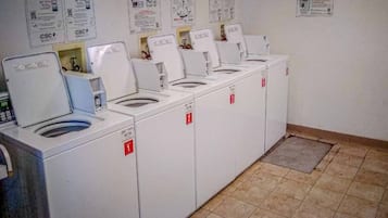 Eine Reihe von weißen Wäschemaschinen mit nummerierten Türen, ein gefliester Boden und Informationsplakate an der Wand.