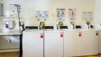 A laundry facility with multiple washing machines, numbered signs, and instructional posters on the wall.