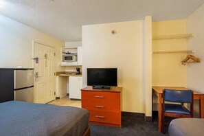 Ett hotellrum med en säng, ett skrivbord med en stol, en tv, en mikrovågsugn och ett kylskåp.