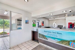 Zona de recepción con un quiosco digital, un cartel grande con el número '6' y un anuncio de una aplicación de reservas.