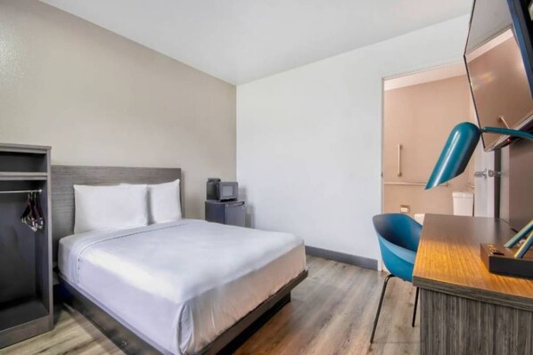 Ein Hotelzimmer mit einem Bett, einem Schreibtisch, einem Stuhl, einem Kleiderschrank und einem Spiegel.