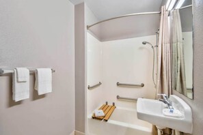 Un baño con ducha, lavamanos y dos toallas en un perchero.