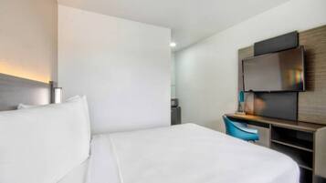 Hotellihuone, jossa on sänky, työpöytä, tuoli, televisio ja pieni pöytä.
