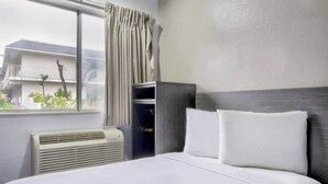 Ett hotellrum med en säng, ett fönster med gardiner, en väggmonterad värmare och utsikt över omgivningen.