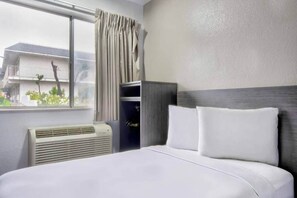 Habitación de hotel con cama, ventana con cortinas, calentador de pared y vista al exterior.