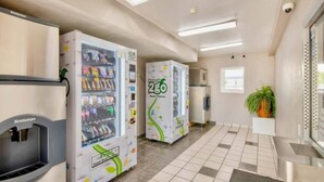 A corridor with vending machines and a push cart, a tiled floor, and a potted plant. - ADA Cozy Full Bed Pool Access (Austin TX)