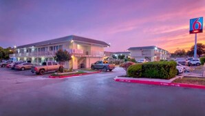 A motel with a parking lot, a sign for the number 6, and a building with a flat roof. - ADA Cozy Full Bed Pool Access (Austin TX)