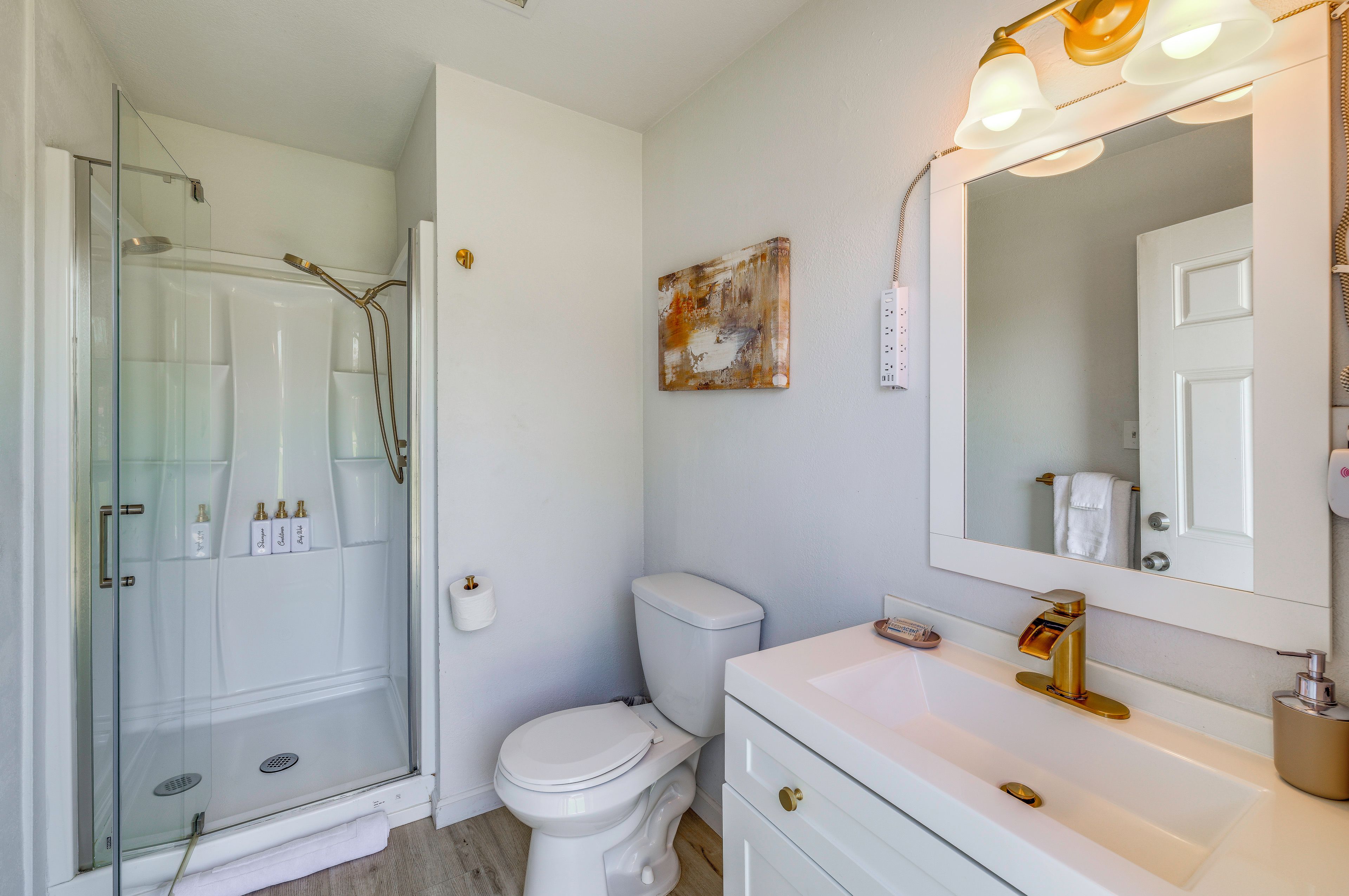 Une salle de bain avec une douche à parois de verre, des toilettes, un lavabo avec un miroir et un luminaire fixé au mur.