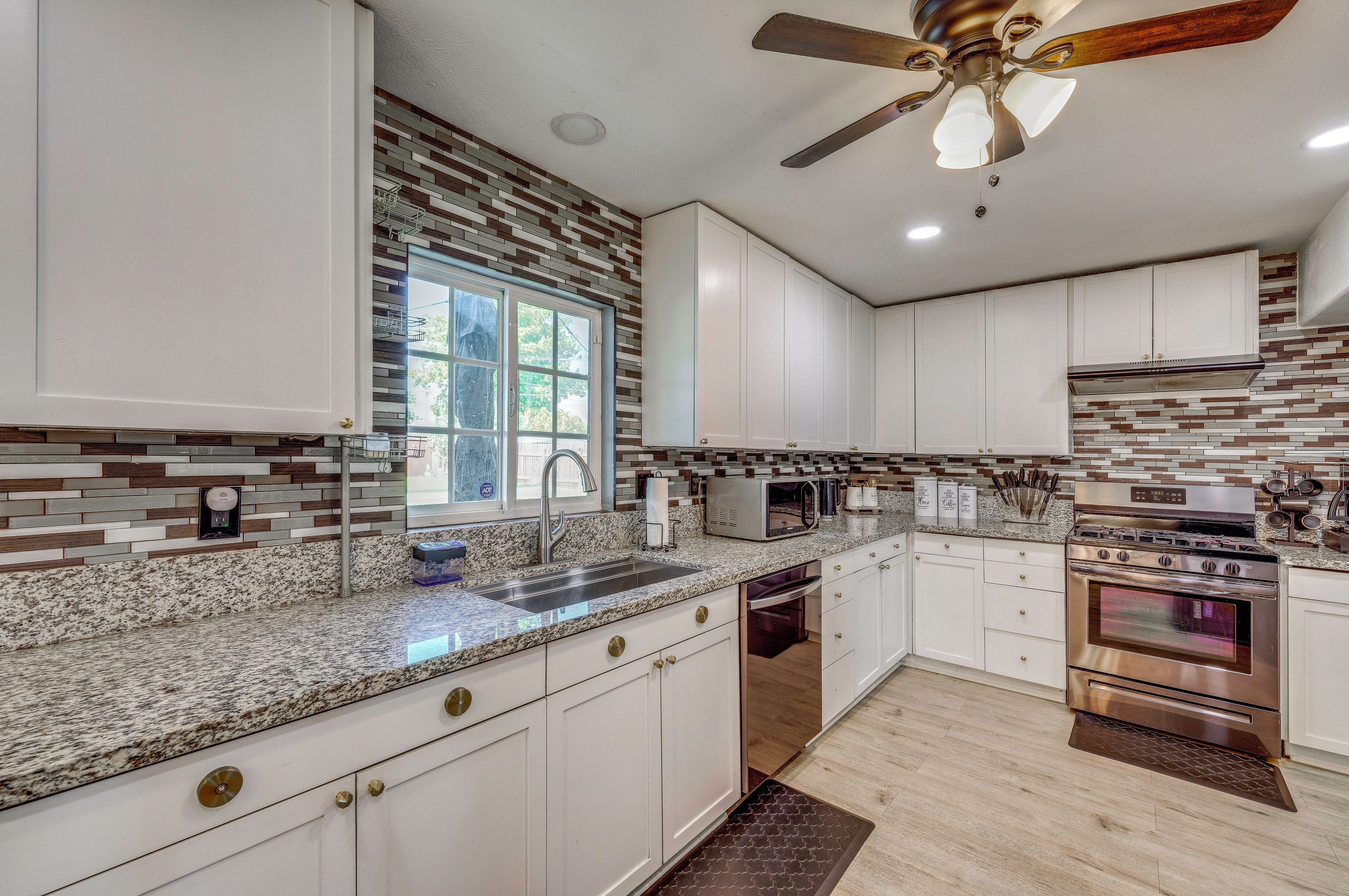 A modern kitchen with white cabinets, a granite countertop, stainless steel appliances, and a window with a view.