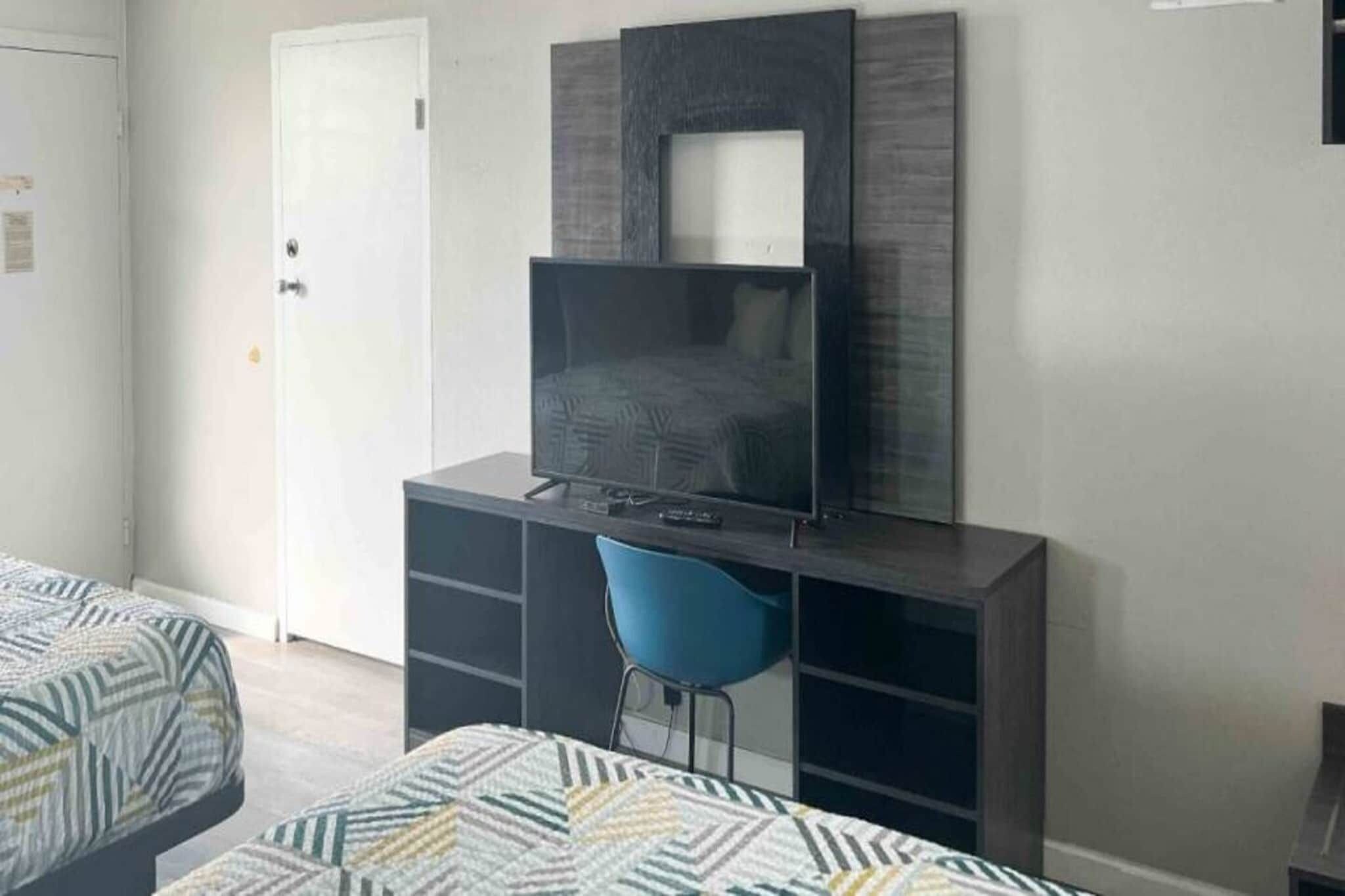 Une chambre à coucher comprenant un lit, un bureau avec une chaise, une télévision et une armoire.
