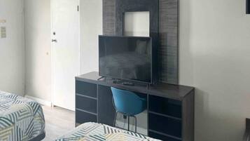 Une chambre à coucher comprenant un lit, un bureau avec une chaise, une télévision et une armoire.