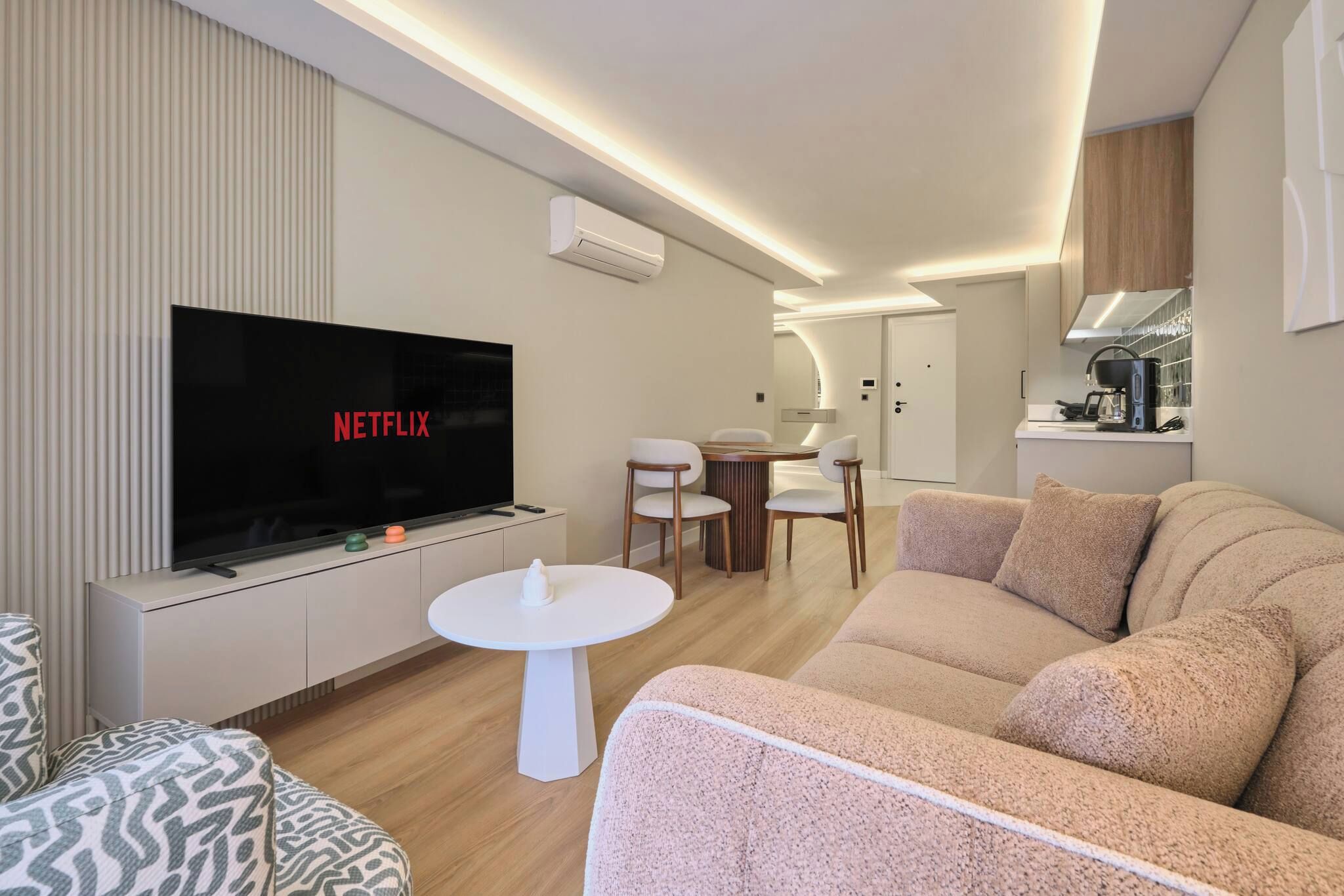 Una sala moderna con un televisor de pantalla plana, un sofá, una mesa de centro y un área de comedor al fondo.