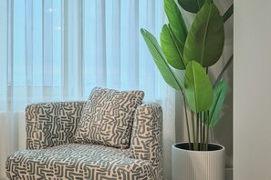 A sofa with patterned cushions and a large potted plant beside a window with sheer curtains. - Tal, 2BR, Premium, Brand New (Kadıköy)