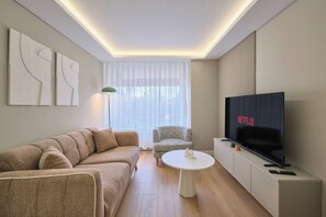 Un salon moderne avec un canapé, un fauteuil à motifs, une table basse et un téléviseur à écran plat.