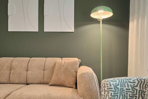 Una habitación con un sofá beige, un otomán estampado, una lámpara de pie y arte abstracto en la pared.