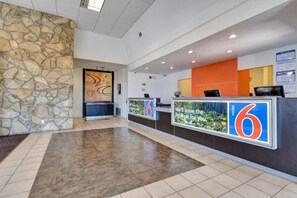 Zona de recepción de hotel con pared de piedra, mostrador de recepción y piso de baldosas.