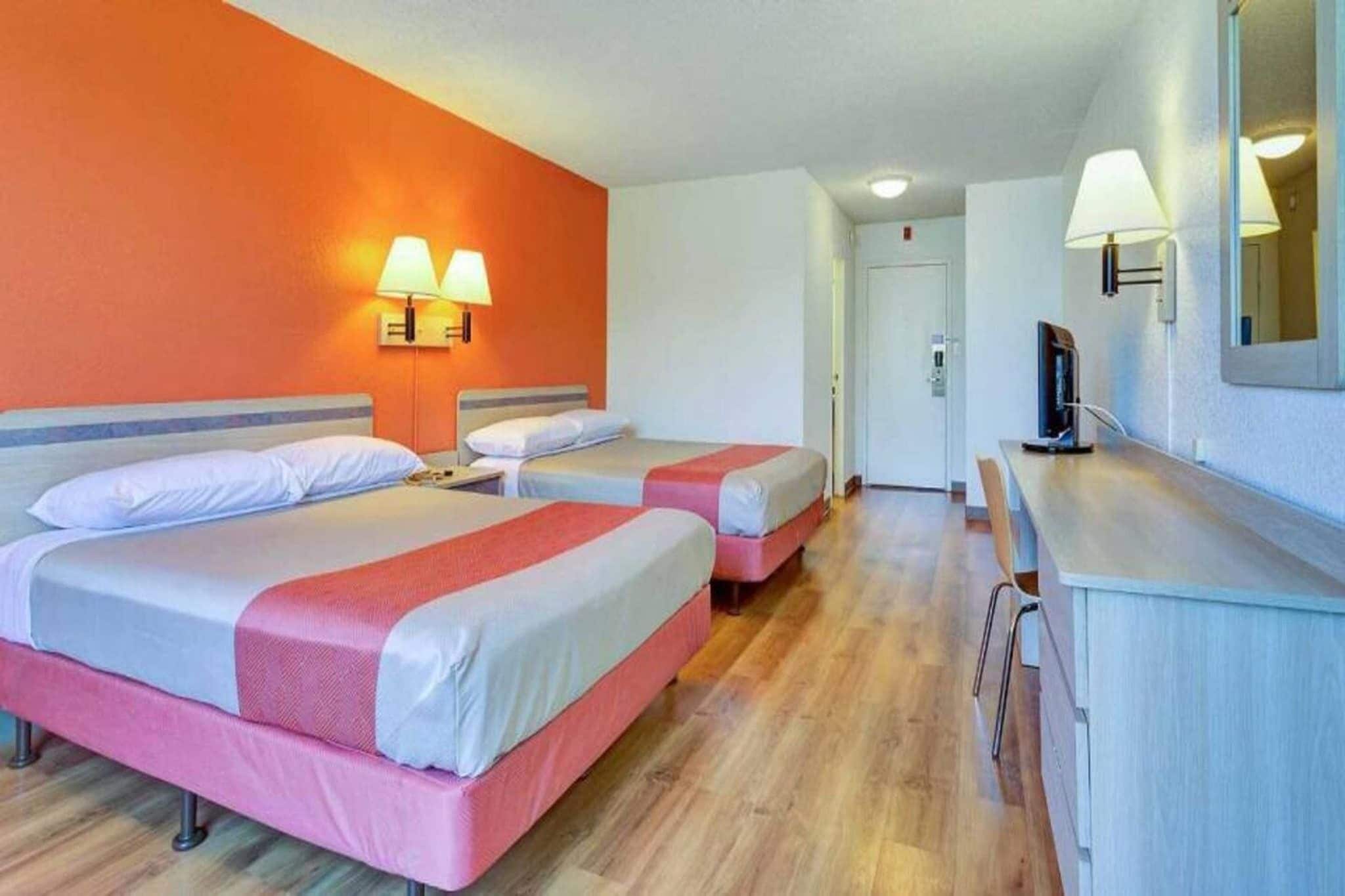 A hotel room with two beds, a desk, and a TV.