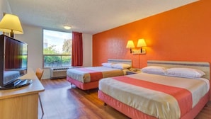 Una habitación de hotel con dos camas, un escritorio con televisor y una ventana con cortinas.