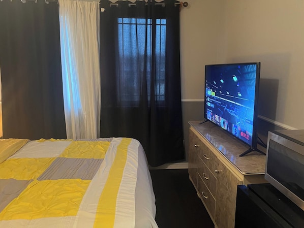 Ein Hotelzimmer mit einem Bett, einem Fernseher auf einer Holzkommode und einem Fenster mit Vorhängen.