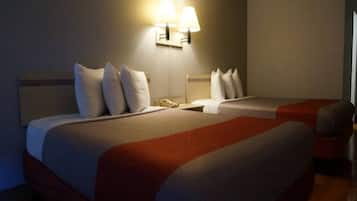 Habitación de hotel con dos camas, cada una con ropa de cama blanca y un detalle rojo. Dos lámparas de pared proporcionan iluminación.