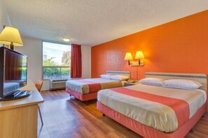 Una habitación de hotel con dos camas, un escritorio con televisor y una ventana con cortinas.