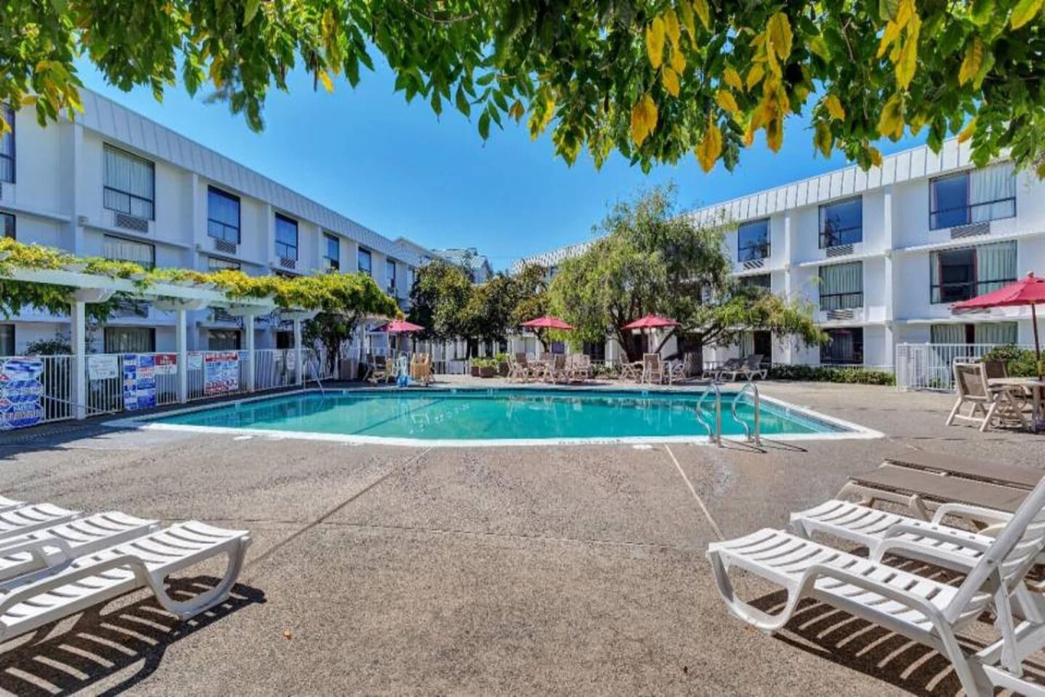 A pool area with lounge chairs and umbrellas, surrounded by multi-story buildings.