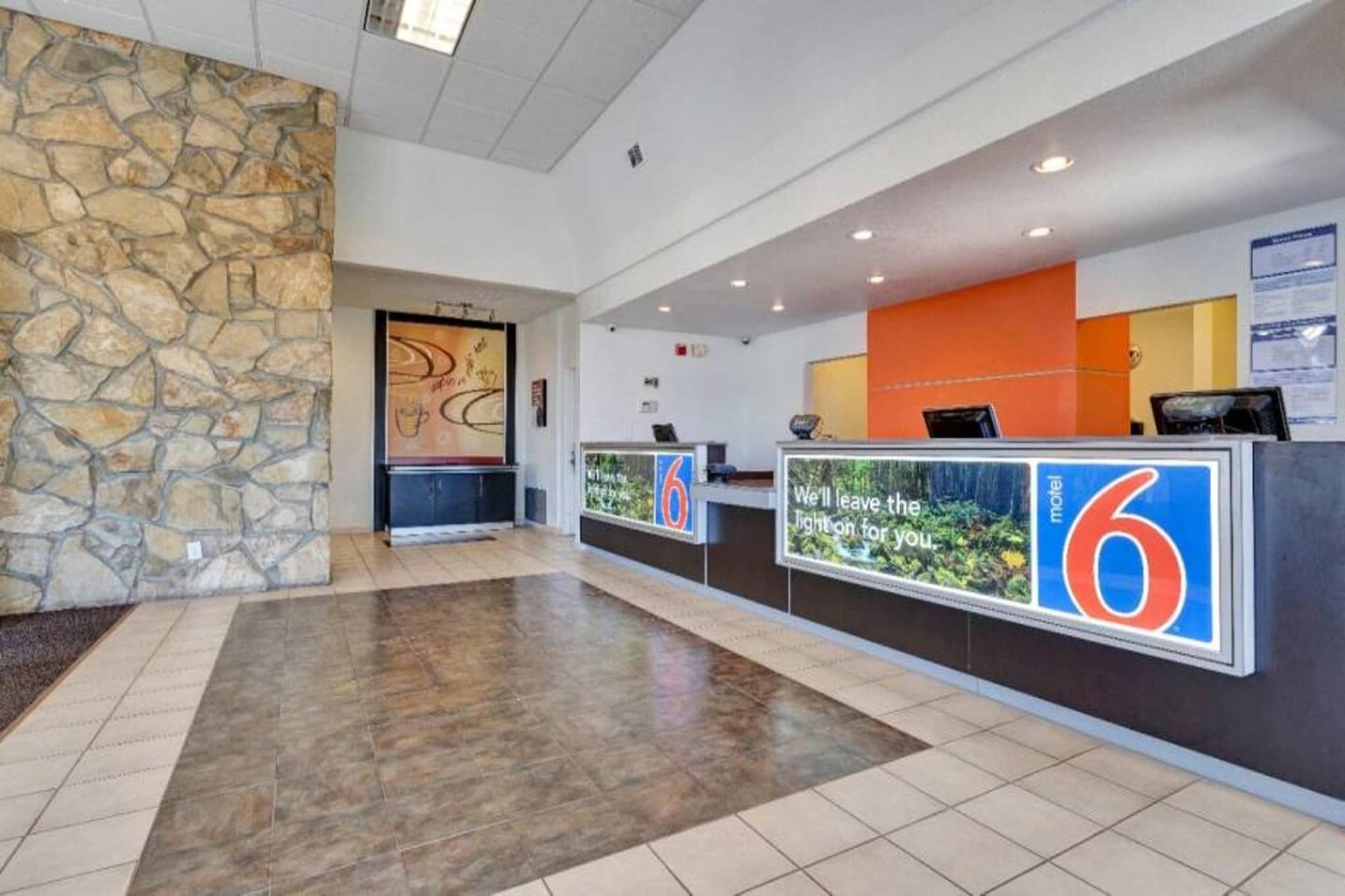 Zona de recepción de hotel con pared de piedra, mostrador de recepción y piso de baldosas.