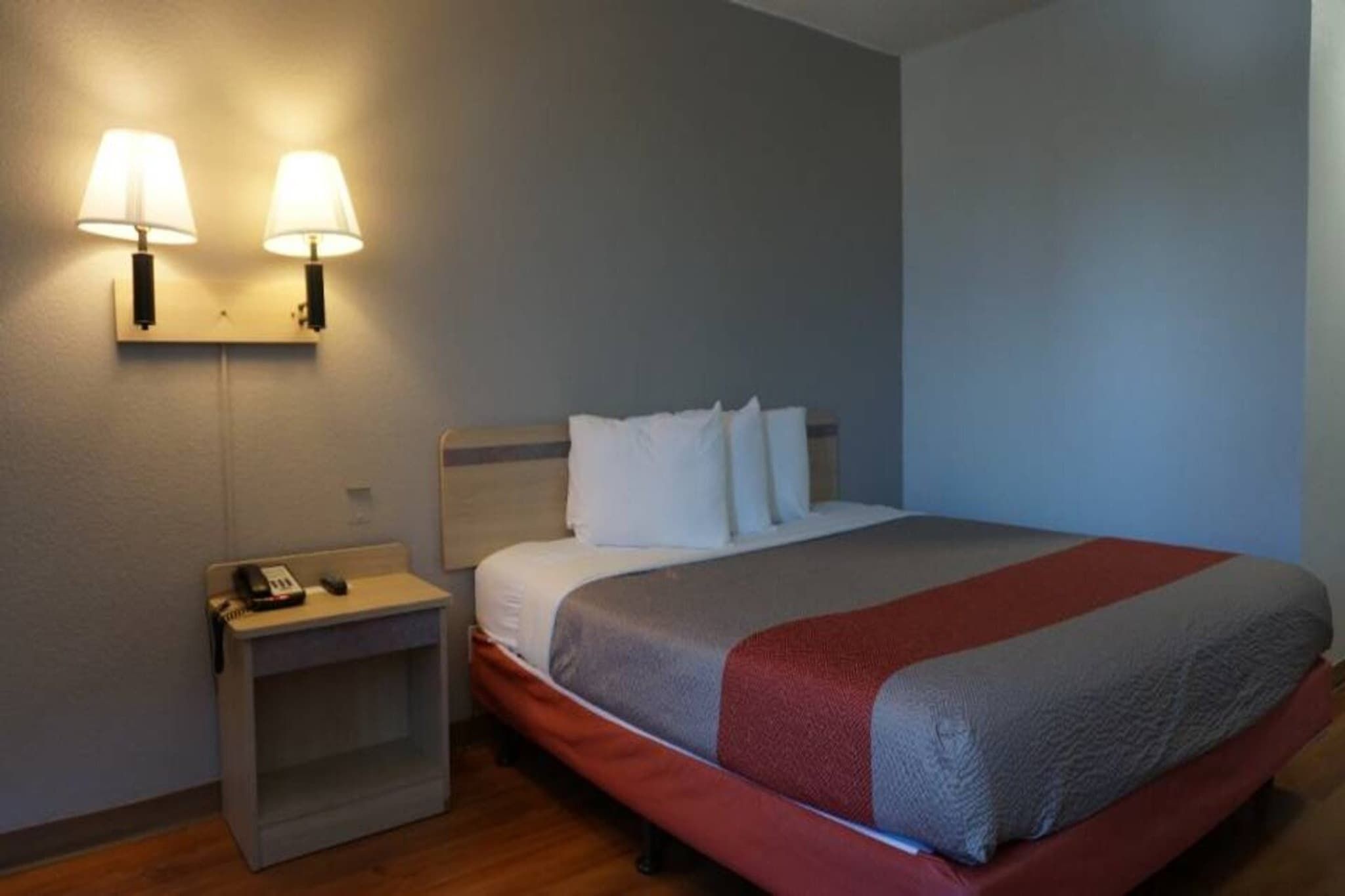 A hotel room with a bed, a nightstand, a telephone, and two wall-mounted lamps.