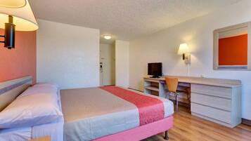 A hotel room with a bed, desk, chair, and a television.