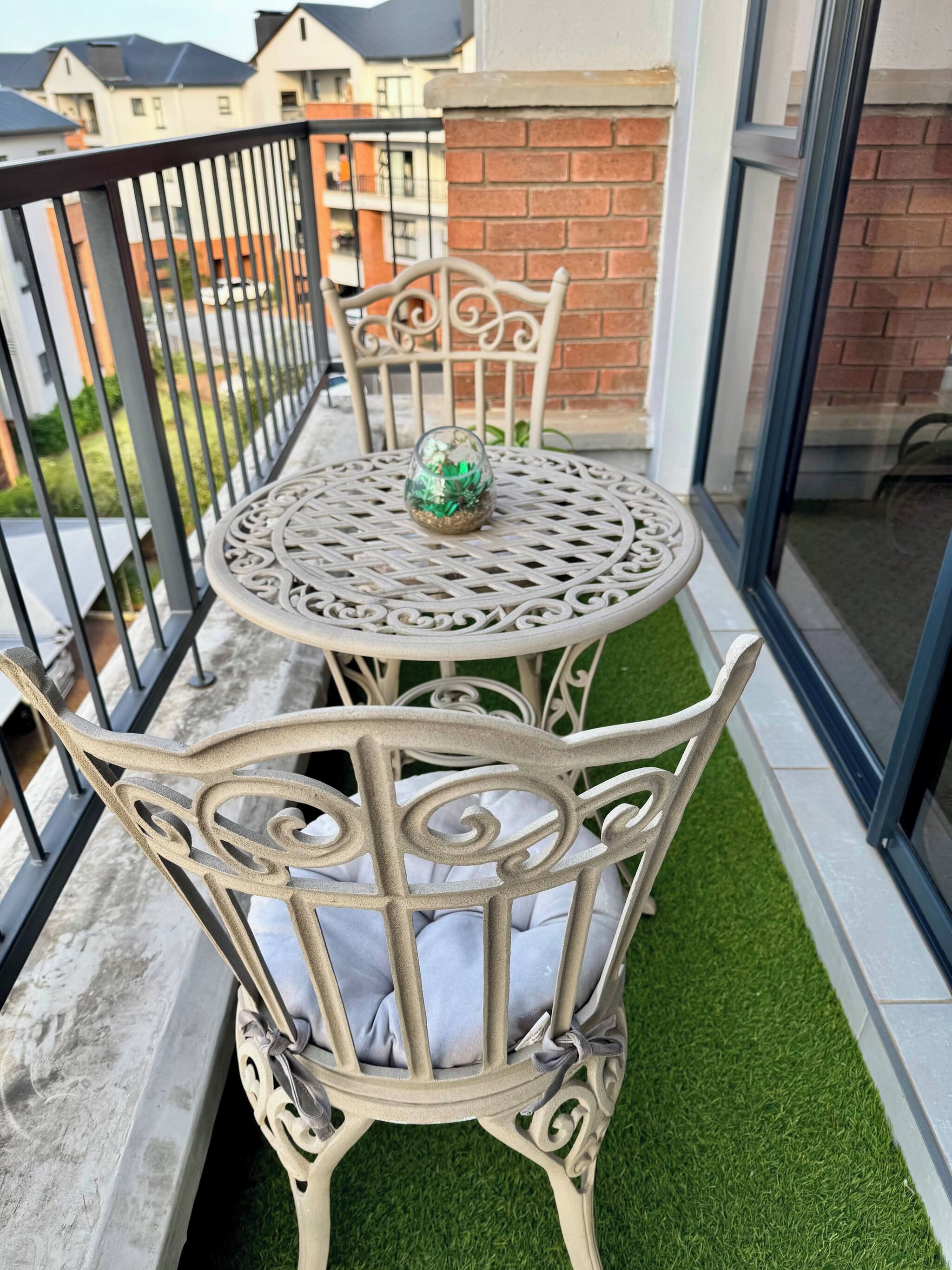 A balcony with a round table and chairs, a glass door, and a view of buildings in the background.