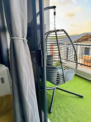 Una habitación con una silla colgante, una cortina y una ventana con vista a un edificio.