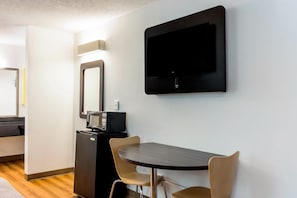 Una habitación moderna con una mesa de comedor, sillas, un televisor montado en la pared, un microondas y un refrigerador.
