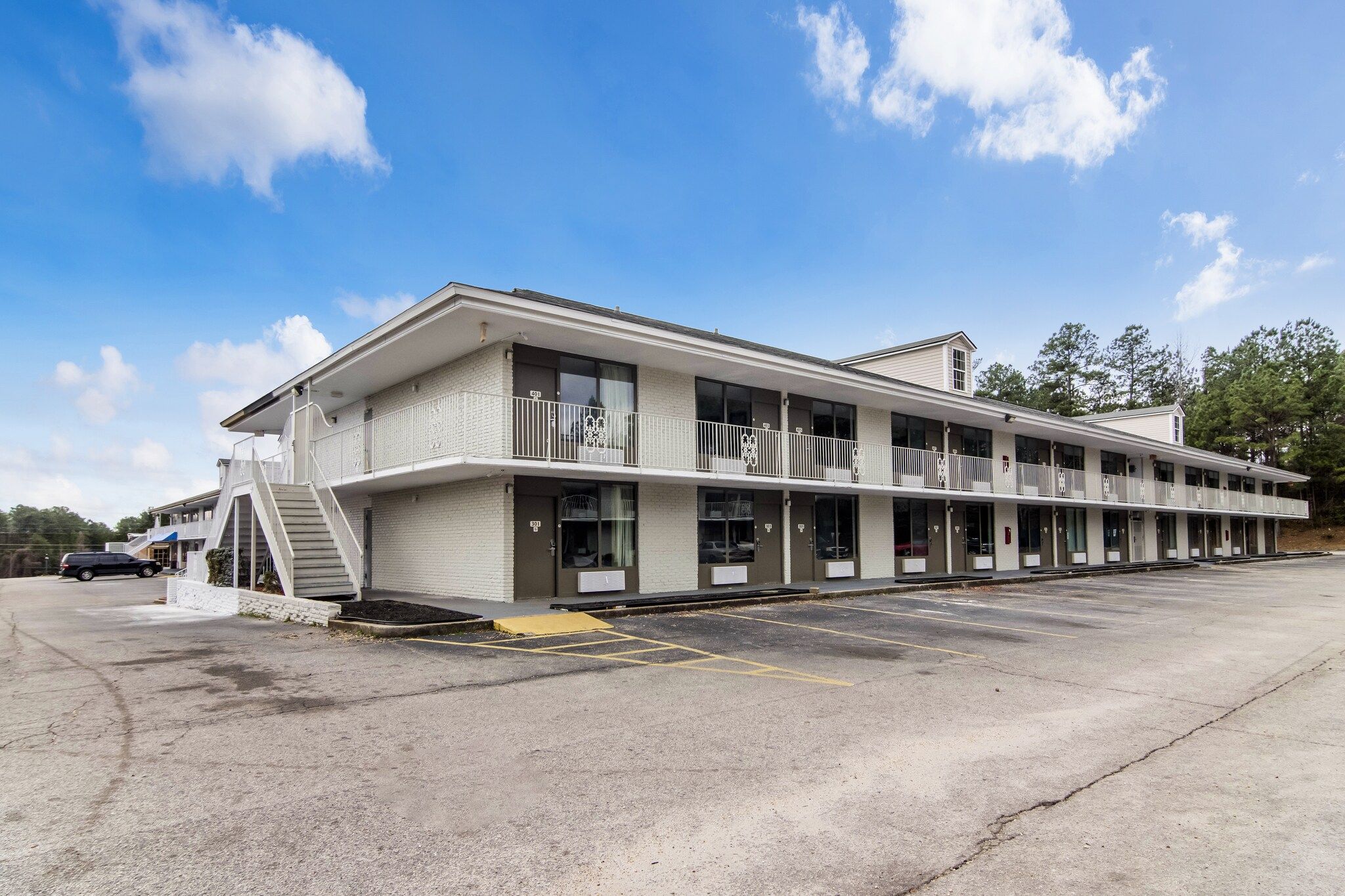 Een motel met twee verdiepingen, een centrale ingang, een overdekte parkeerplaats en een trap naar de bovenverdieping.