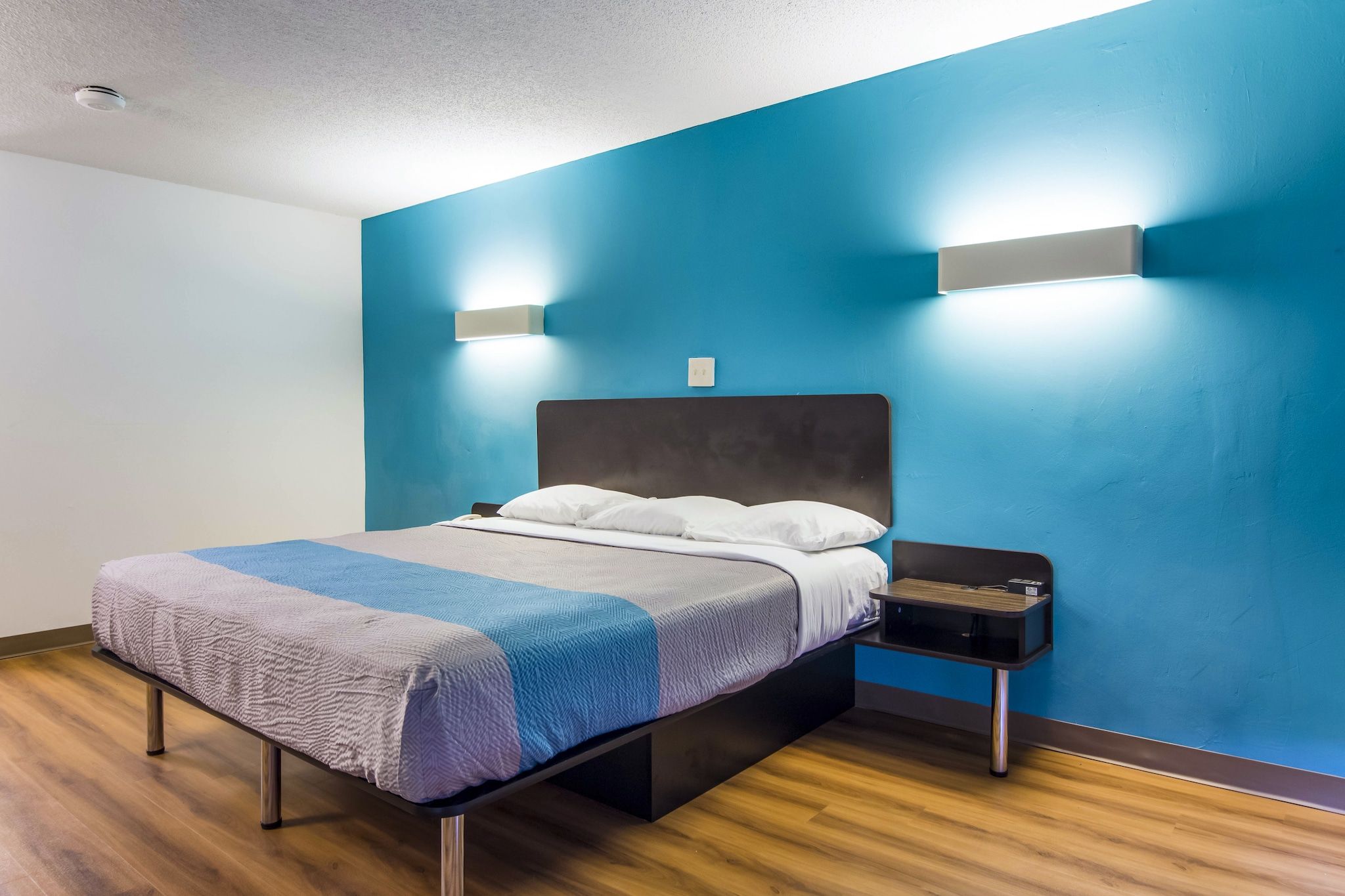 Une chambre d’hôtel moderne, équipée d’un lit, d’une table de chevet et d’un luminaire fixé au mur.