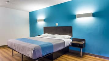Une chambre d’hôtel moderne, équipée d’un lit, d’une table de chevet et d’un luminaire fixé au mur.