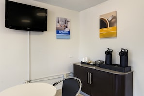 Habitación de hotel con televisor de pantalla plana, escritorio con silla, cafetera y un mueble con un cartel en la pared.