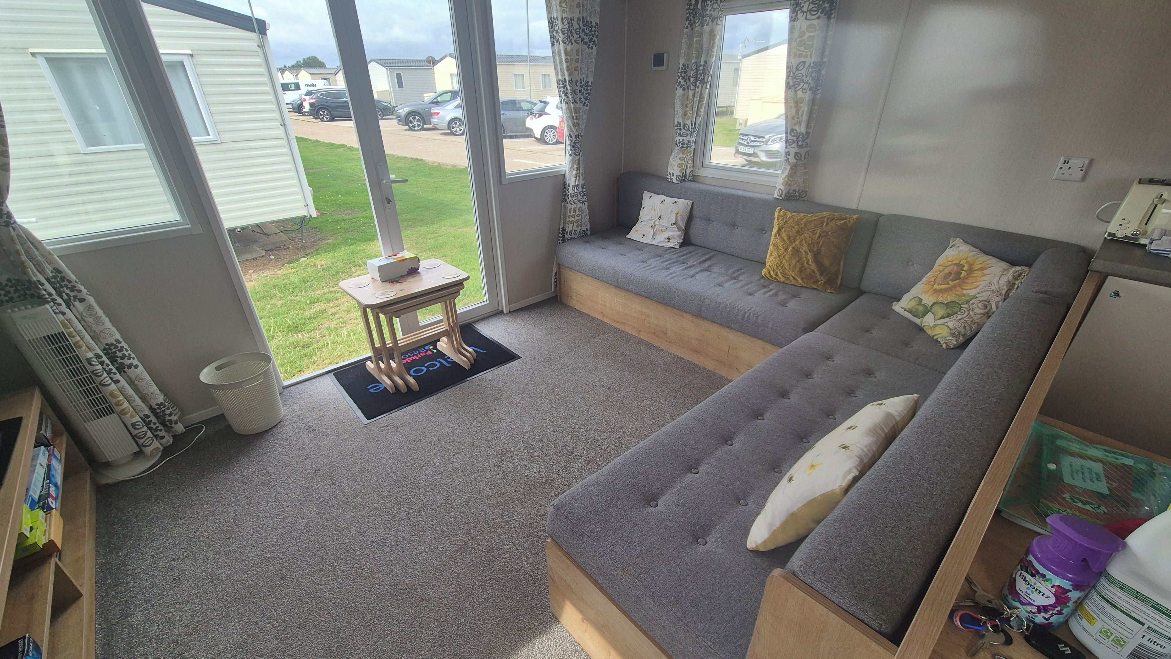 Ein Wohnzimmer mit grauem Sofa, einem kleinen Tisch und Blick ins Freie.