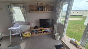 Ein Wohnzimmer mit Fernseher, Bücherregal und Blick auf eine Rasenfläche.