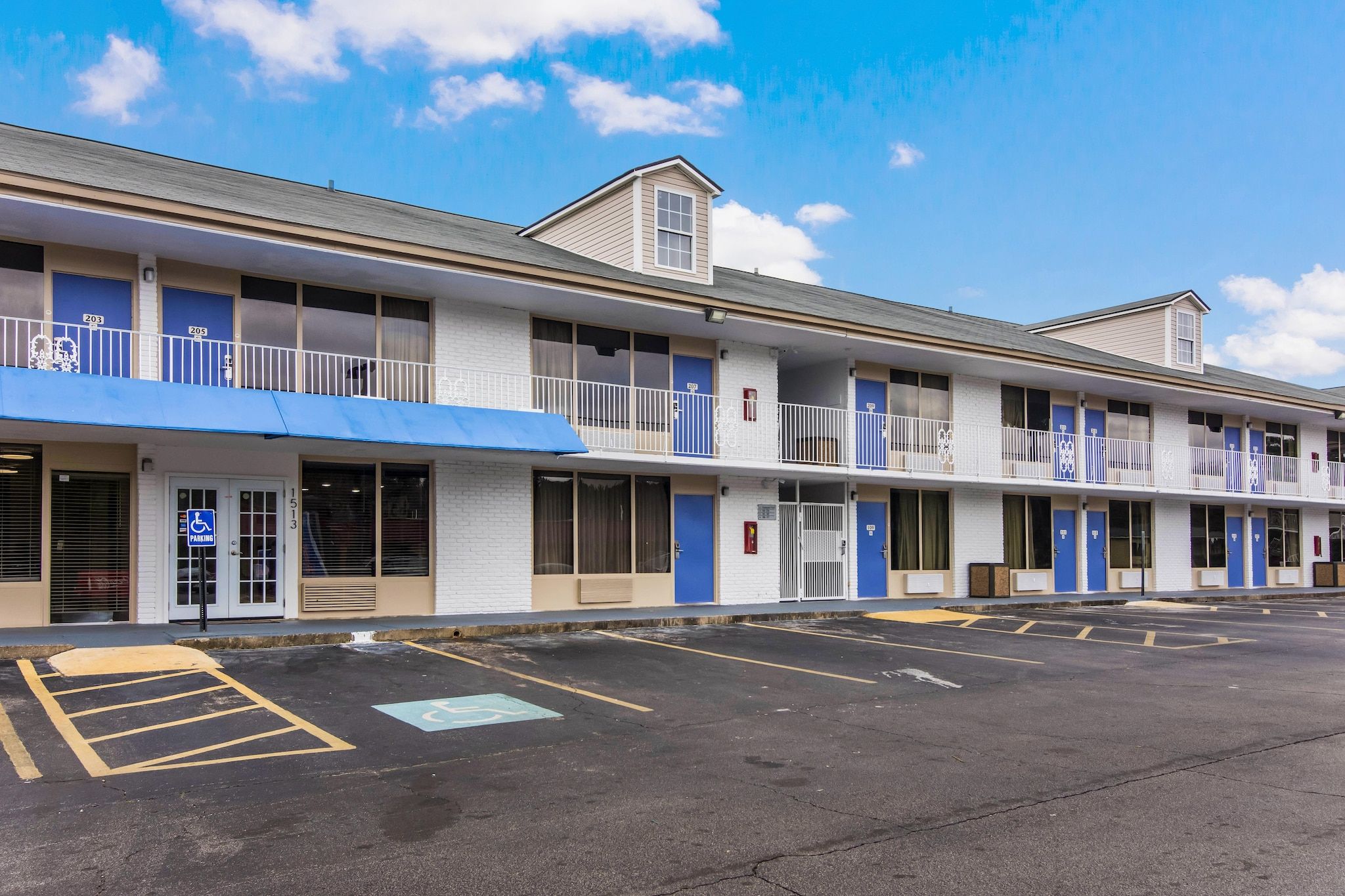 Een motel met meerdere kamers, een parkeerplaats en een blauw afdak.